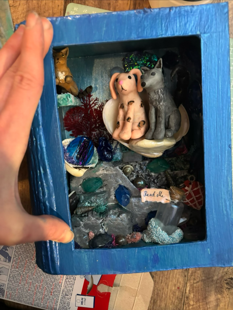 A handmade book looking thing with a miniature underwater world inside it. There are reason crystals and a bunny and a wolf.